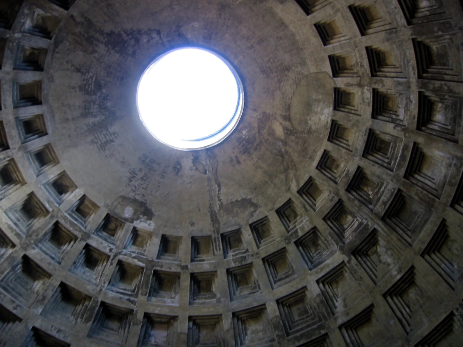 Looking straight up inside the Pantheon at the concrete dome: rings of square coffers, each stepped inward, narrowing toward the bright round opening of the oculus at the top