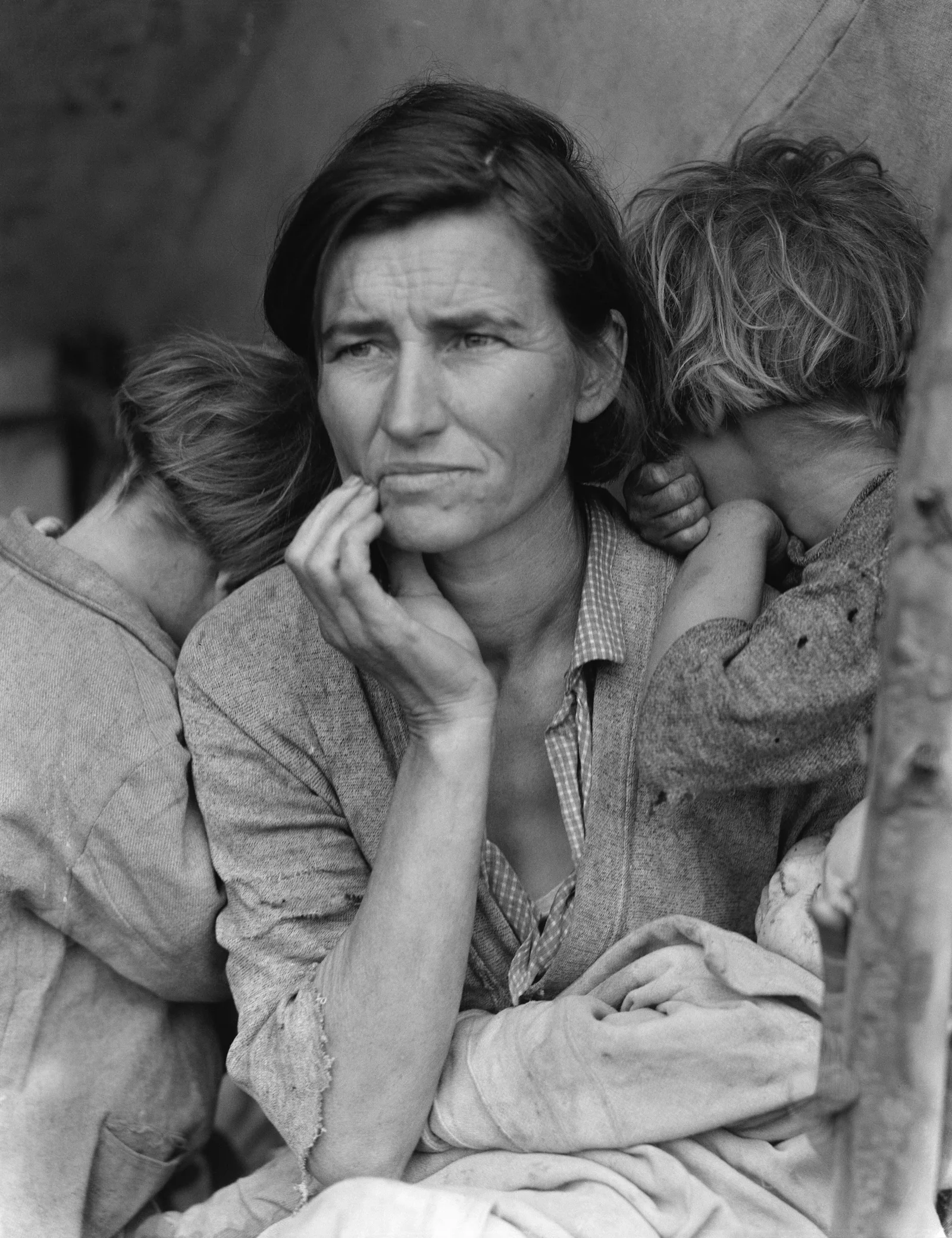Black-and-white photograph of a careworn woman holding a hand to her chin, with two children turning their faces away over her shoulders and a baby in her lap